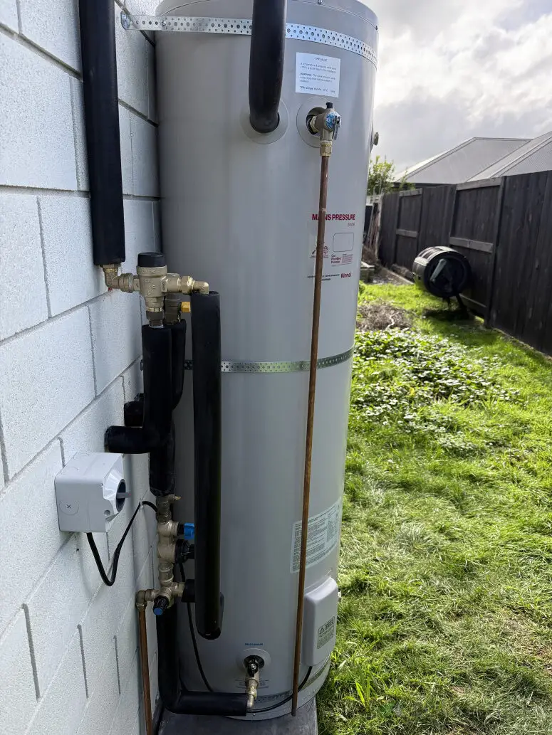 Outdoor hot water cylinder on a block wall, replaced and plumbed by Tron Plumbing